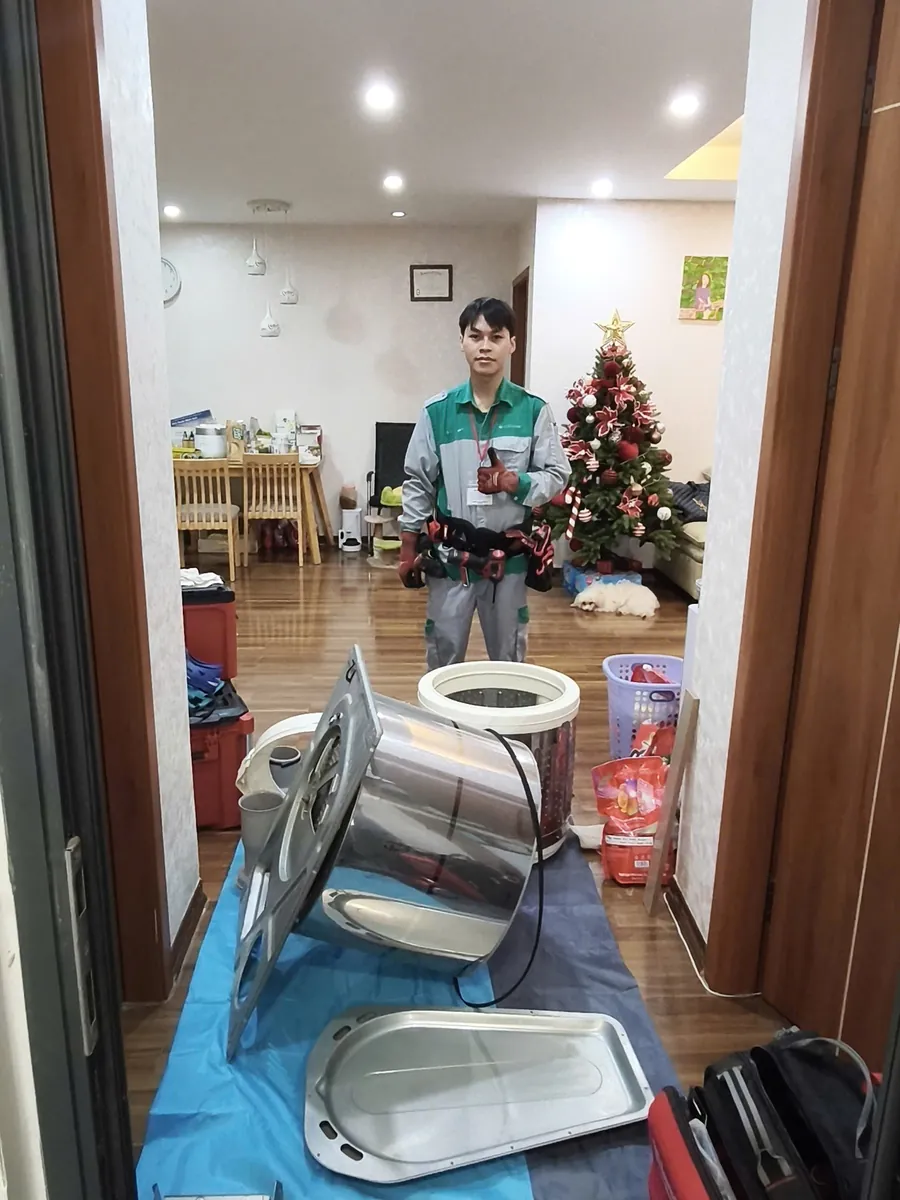 Kỹ thuật viên CareHome bên cạnh các bộ phận máy giặt đã tháo, có bạt che chắn